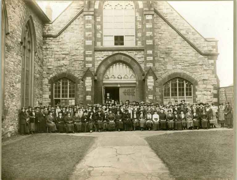 Black and white photograph of stone church with large crowd of people out front