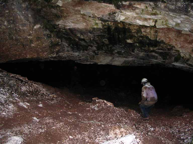 Photographie couleur d’un homme penché, en salopette et casque de protection, qui entre dans une caverne de gypse