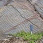 Photographie couleur de roche grise avec stries diagonales et marteau comme valeur d'échelle