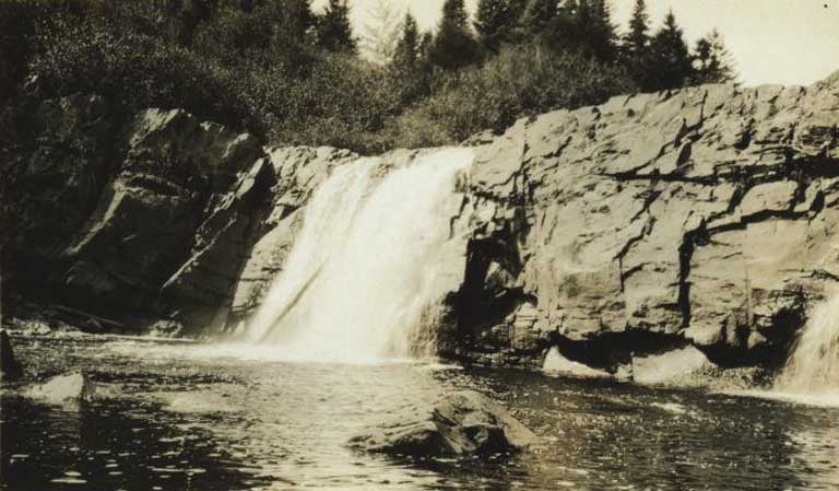 Photographie noir et blanc d’une chute d’eau avec corniches rocheuses et rivage