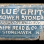 Photographie couleur d’une étiquette « Blue Grit Mower Stone » (pierre à affûter en grès grossier bleu) sur une roche grise