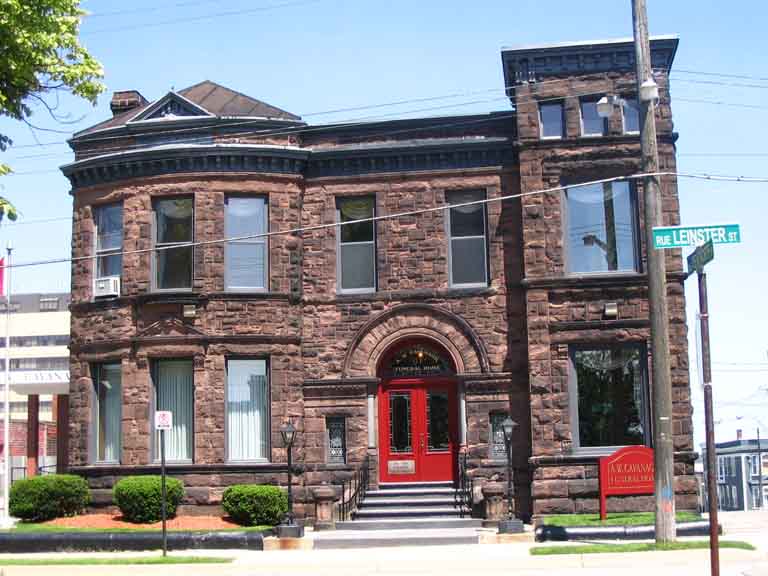 Photographie couleur d’une maison rouge en pierre à deux étages avec des fenêtres donnant sur la rue