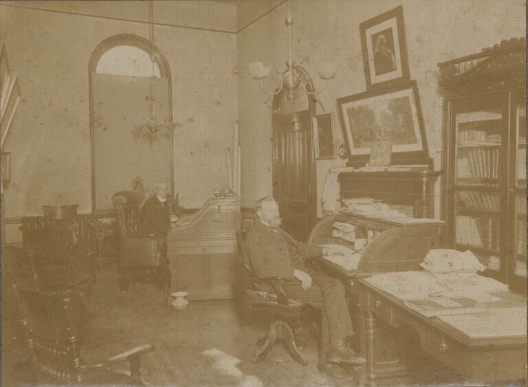 Photographie noir et blanc de deux hommes assis à un bureau dans un ancien bâtiment