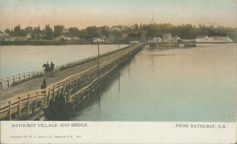 Carte postale couleur montrant un pont étroit emprunté par des passants, des chevaux et une charrette et, en arrière-plan, un quai et le village