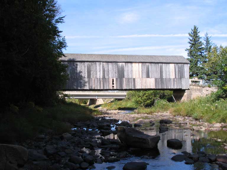Colour photograph of wooden covered bridge over a rocky stream
