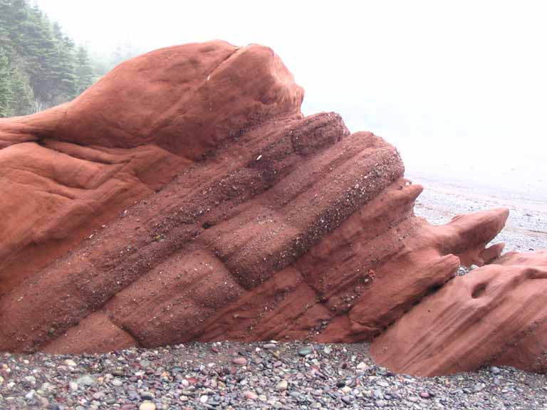 Colour photograph of a red sandstone rock on the beach