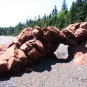 Colour photograph of a red sandstone rock on the ocean with a beach and trees on top of the cliff