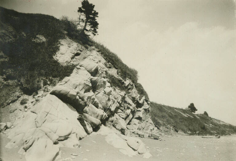 Photographie noir et blanc d’une falaise rocheuse sur une plage
