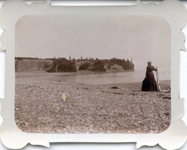 Photographie noir et blanc d’une femme sur une plage avec une falaise rocheuse à l’arrière-plan