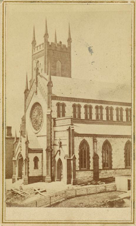 Black and white photograph of stone church with round window over entry and steeple on left