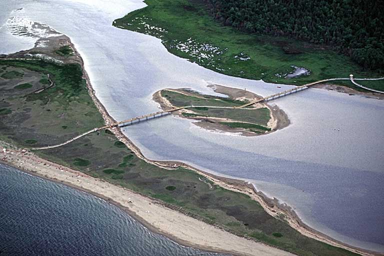 Photographie couleur d’un pont qui relie des plages avec de la végétation verdoyante et l’eau bleue de l’océan