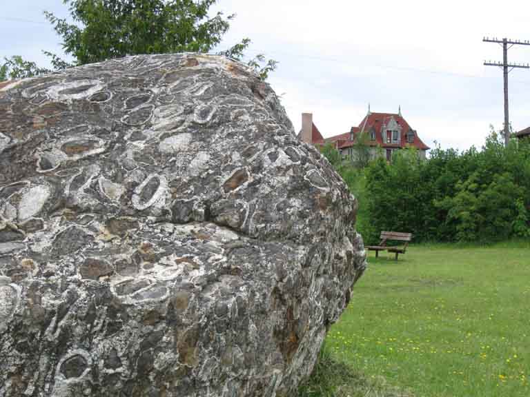 Colour photograph of a large gray rock boulder on green grass with a building in the background