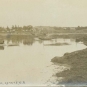 Carte postale noir et blanc montrant un rivage rocailleux à marée basse, l'eau, des bateaux et des maisons
