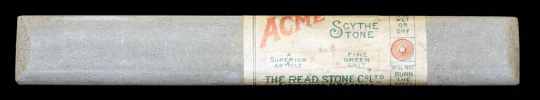 Colour photograph of a long gray stone with a label ‘ACME Scythe Stone’