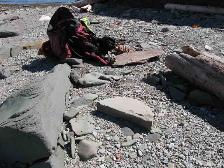 Colour photograph of rocks on a beach with a backpack and half of a circular gray stone