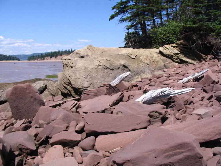 Colour photograph of a beach with block of red and gray rocks