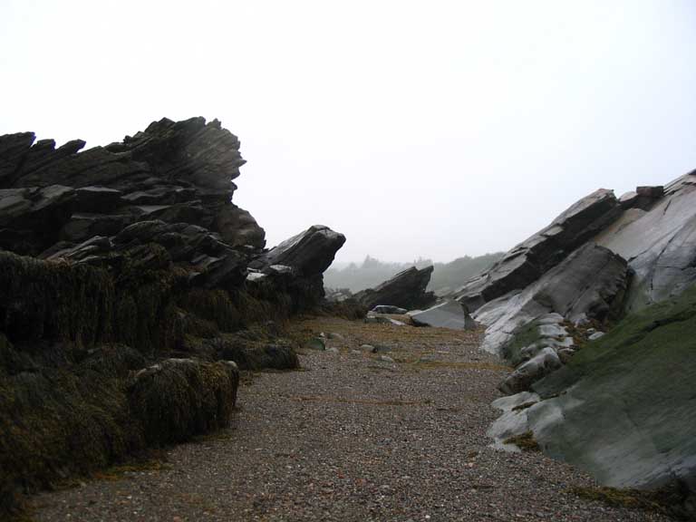Colour photograph of layers of rocks jutting out of the beach on the shore