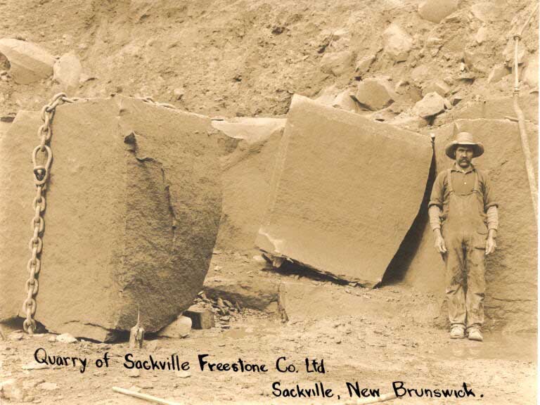 Black and white photograph of a man standing in front of large sandstone blocks in an old quarry