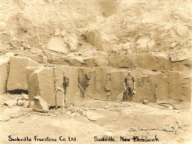 Black and white photograph of a man standing in front of large sandstone blocks in an old quarry