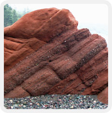 Photographie couleur d’une roche en grès rouge sur la plage