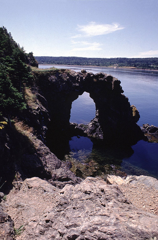 Colour photograph of curved rock formation with hole in the middle on shoreline
