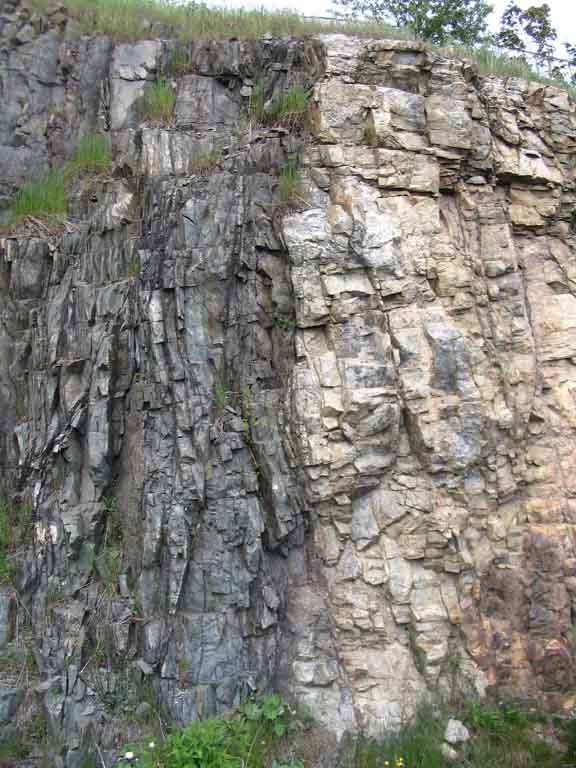 Colour photograph of rock face with dark gray rock of one formation on left and light gray rock of another formation on the right