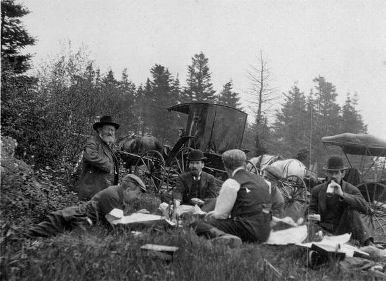 Black and white photograph of camp site with five men, carriages and horses