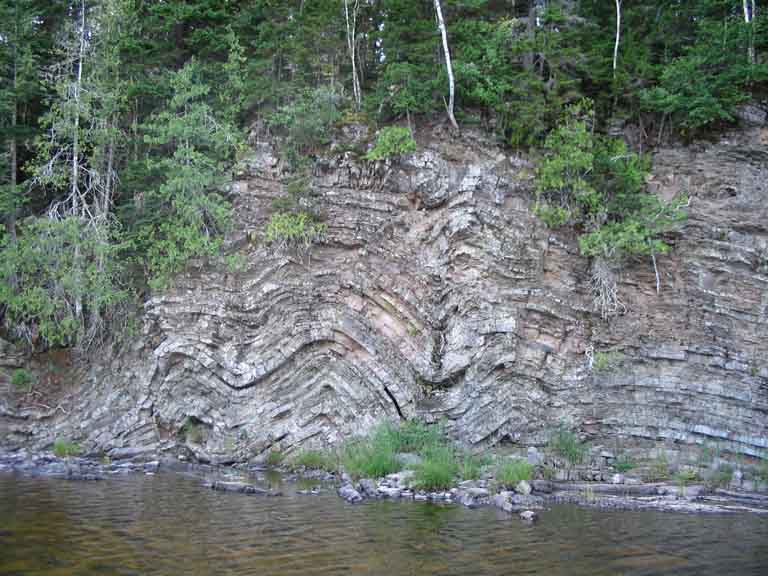 Colour photograph of water, rock face with horizontal lines and trees