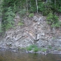 Colour photograph of water, rock face with horizontal lines and trees