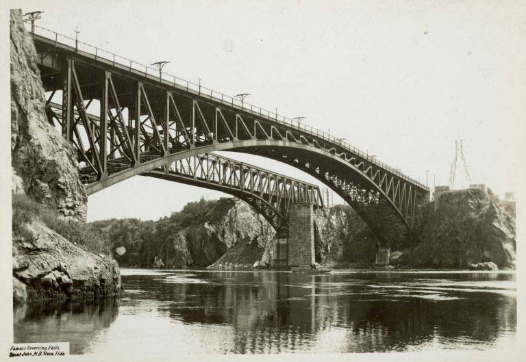 Photographie noir et blanc de cours d’eau, falaises rocheuses et ponts en acier vus d’en dessous