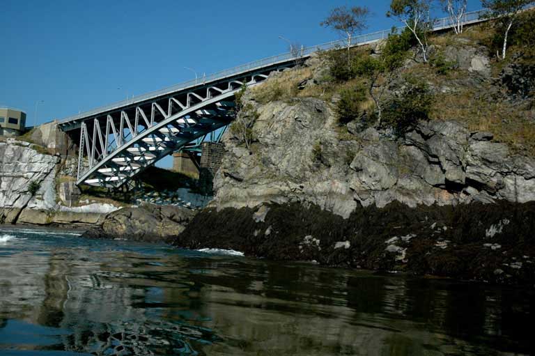 Photographie couleur d’un pont à charpente métallique enjambant un cours d’eau et d’une paroi rocheuse