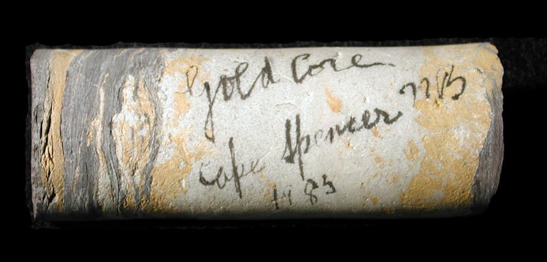Photographie couleur d’une roche blanche, jaune et grise qui porte l’inscription « Gold Core Cape Spencer 1983 » (carotte de la mine d’or de Cape Spencer) 