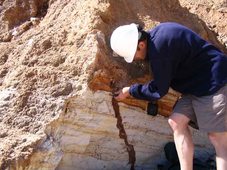 Colour photograph of a man standing in front to a brown and white rock