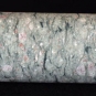 Colour image of round, tube-like sample of gray rock mottled with white and pink rock