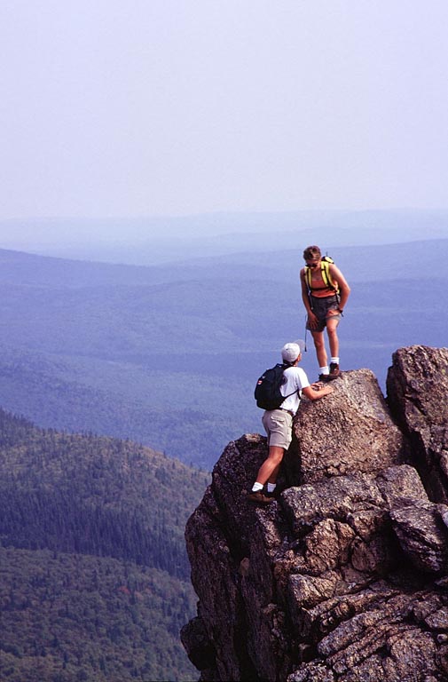 Colour photograph of two people at rock summit of mountain