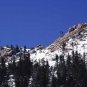 Colour photograph of rocky mountain peak with trees, snow and building