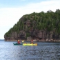 Colour photograph of two kayaks on calm water near rocky peninsula with trees