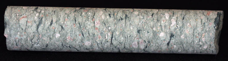 Image couleur d’un échantillon de roche grise en forme de tube marbré de blanc et de rose