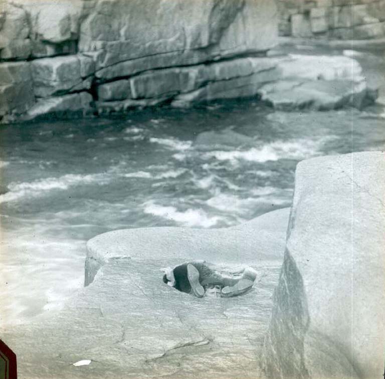 Image couleur d’une rivière et d’une ligne de rivage rocheuse et d’un homme glissé dans un trou laissant voir seulement sa tête et ses pieds 