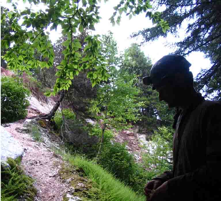 Colour photograph of rocky hillside with grass and trees and person with hard hat with light attached
