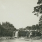 Black and white photograph of waterfall and rocky ledges and shoreline in distance
