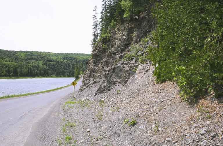 Colour photograph of rock face, trees, road and river