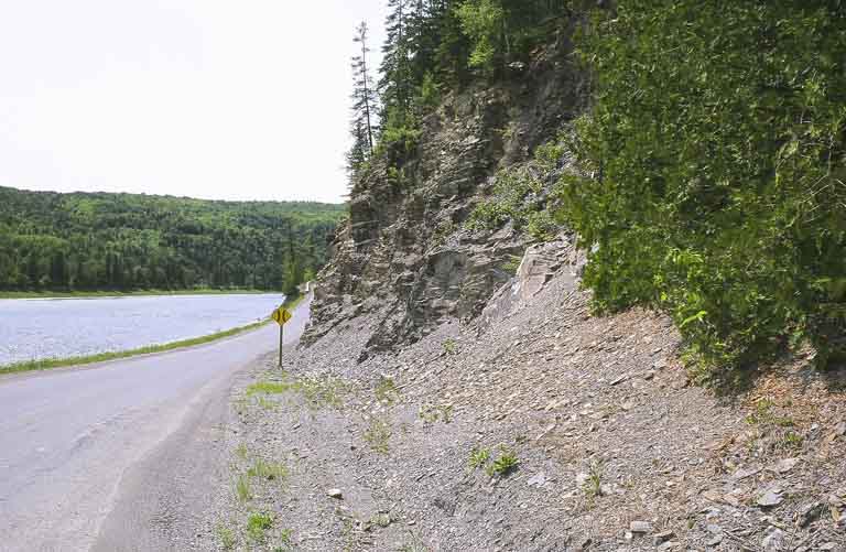 Photographie couleur d’une paroi rocheuse, d’une route, d’arbres et d’une rivière