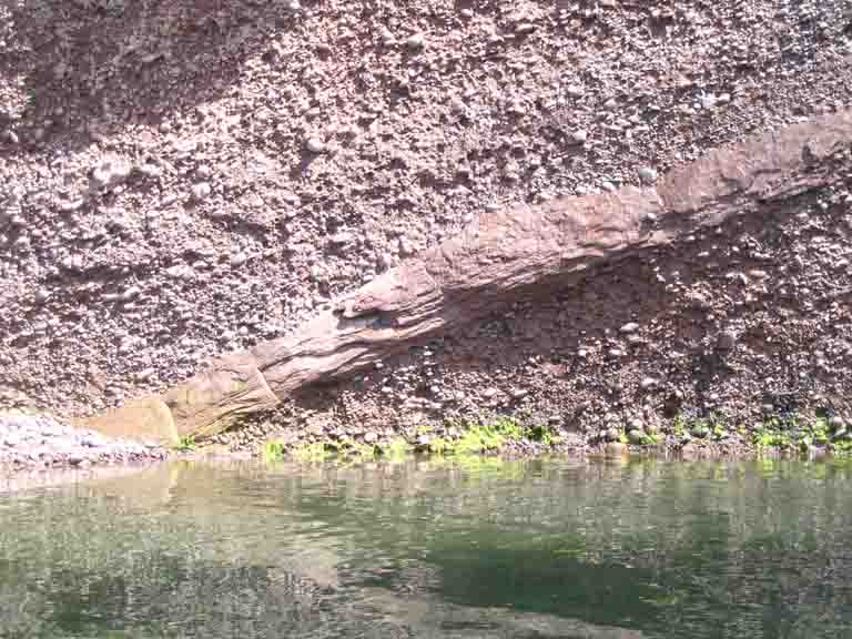 Colour photograph of a brown rock cliff on the ocean