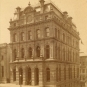Black and white photograph of building with mansard roof, clock and cornice decoration