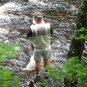 Colour photograph of man standing in a brook