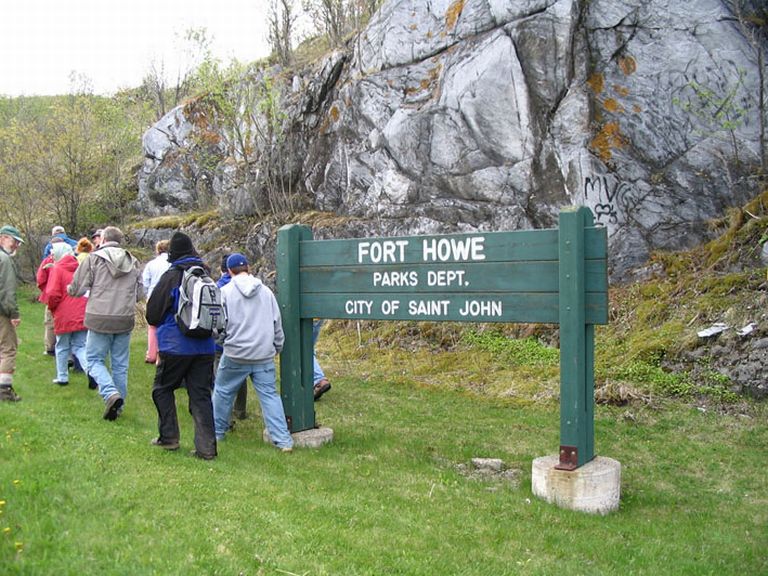 Colour photograph of rock face, people and green sign