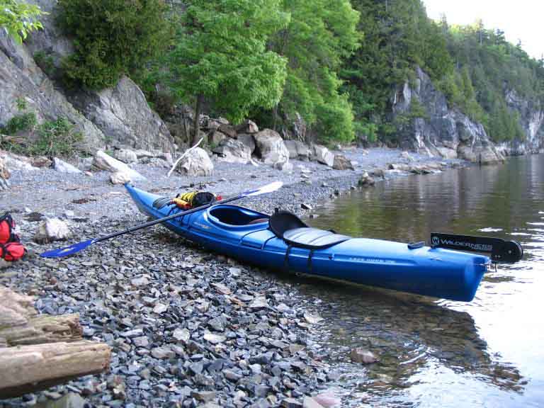 Colour photograph of blue kayak on rocky beach