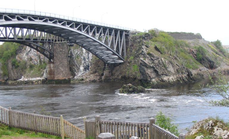 Photographie couleur d’un pont à charpente métallique enjambant un cours d’eau et une paroi rocheuse