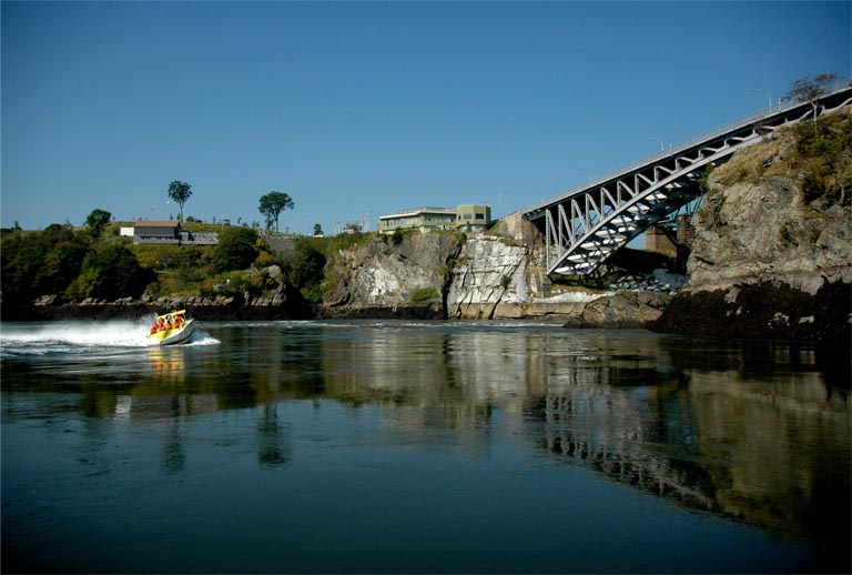 Photographie couleur d’un pont à charpente métallique, d’un cours d’eau et d’une paroi rocheuse 